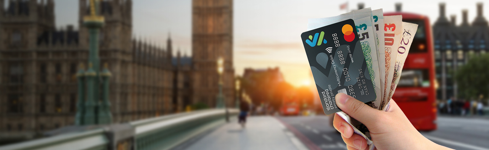 A hand holding a Multi-Currency Mastercard Debit Card and foreign currency against London scenery