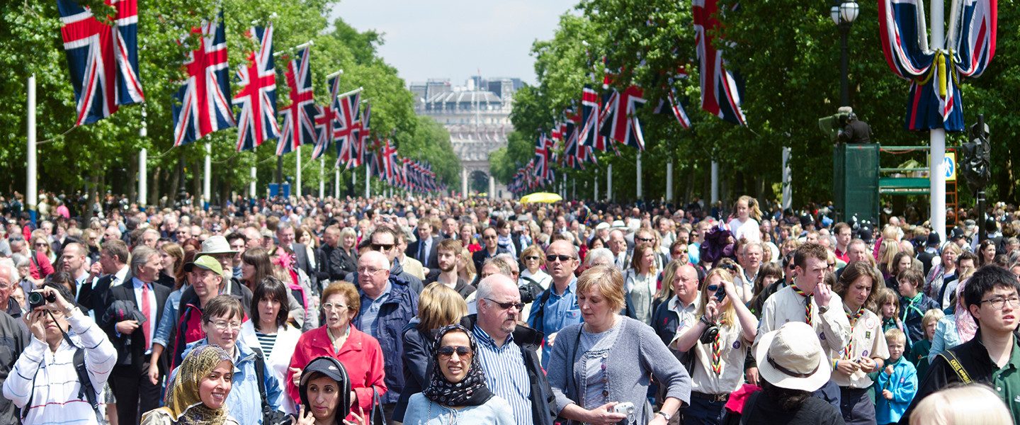 crowd of people along street with trees and union jack flags along the sides