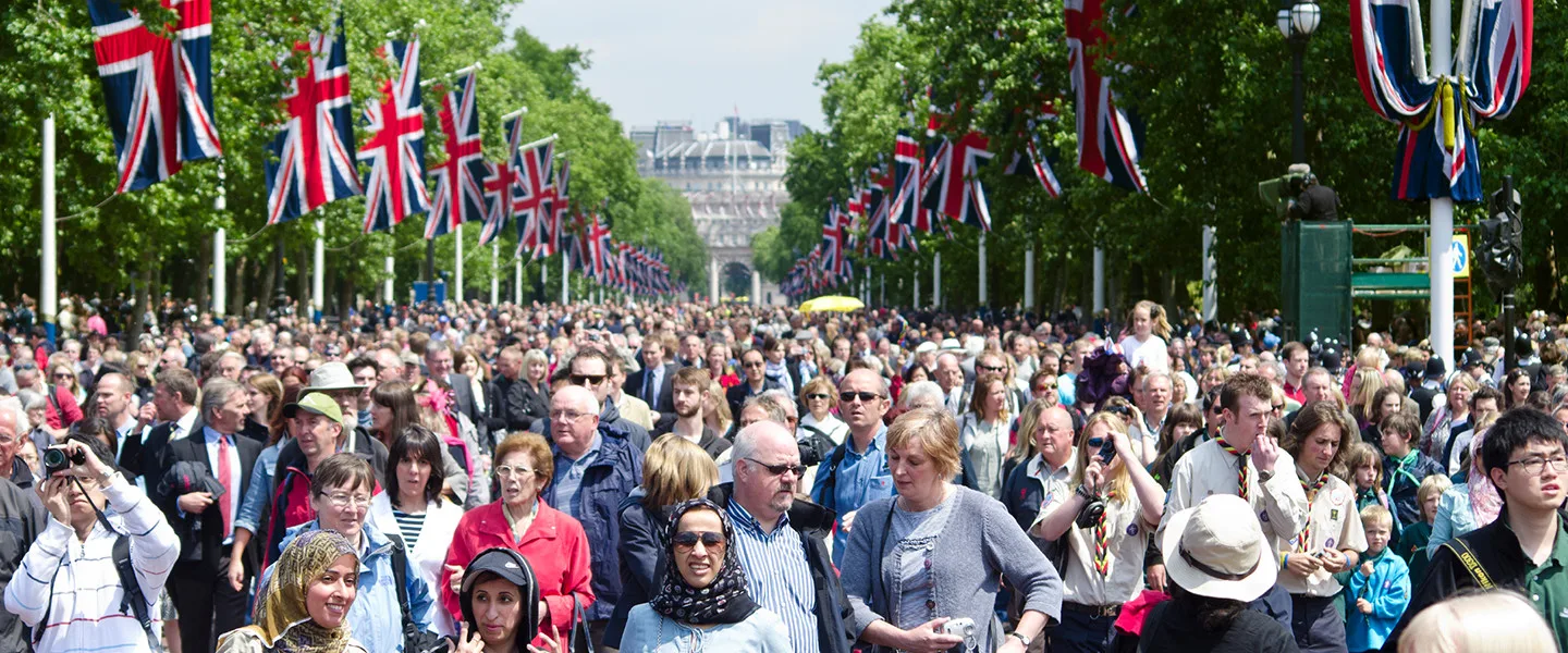 crowd of people along street with trees and union jack flags along the sides