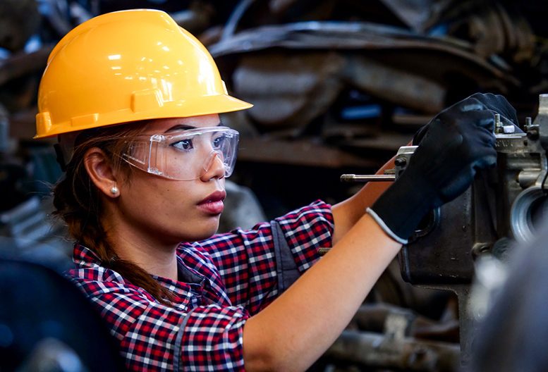 A woman in a hard hat works on machinery.