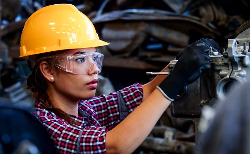 A woman in a hard hat works on machinery.