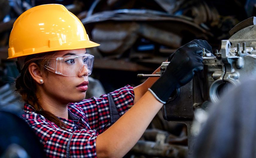 A woman in a hard hat works on machinery.
