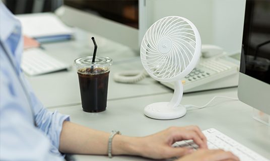 Desk fan next to a computer showing comfortable workplace for menopause symptoms.
