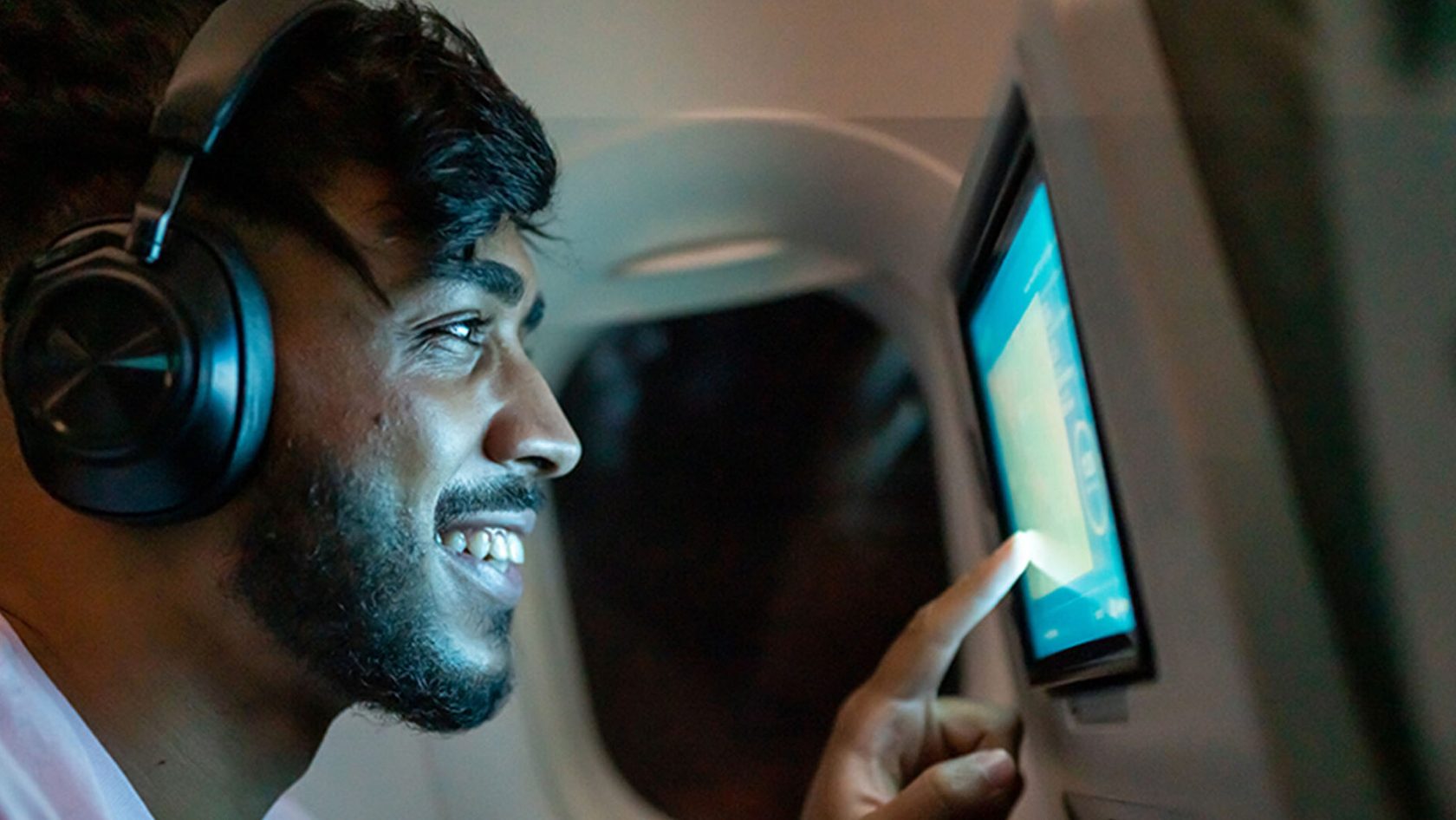 A passenger on a flight smiles as he uses a screen on a seat back