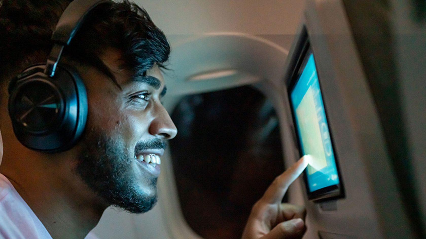A passenger on a flight smiles as he uses a screen on a seat back