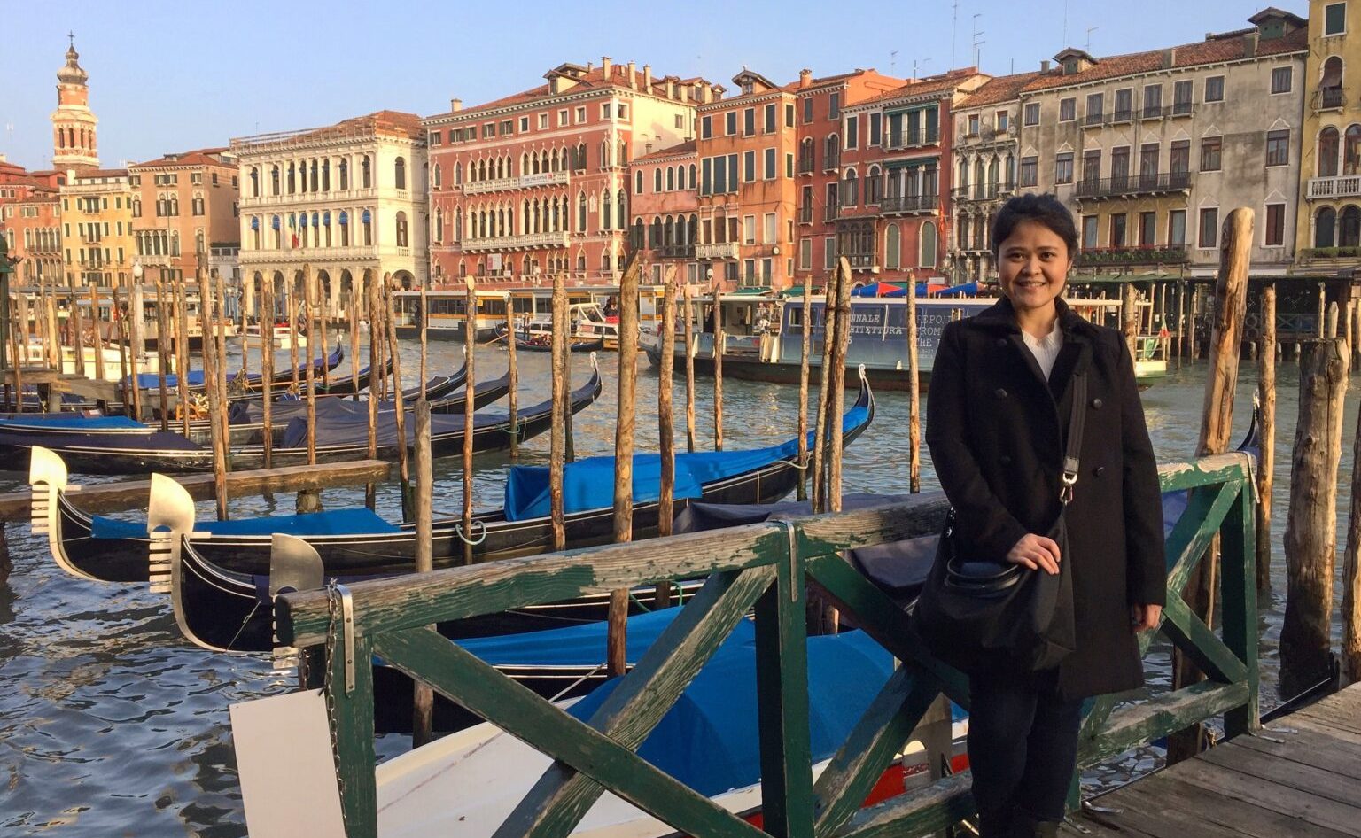 A woman standing near a water canal lined with boats