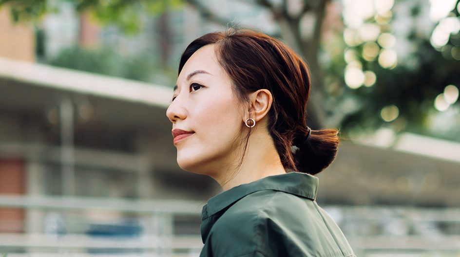 A woman relaxes outside a building on a leafy street.