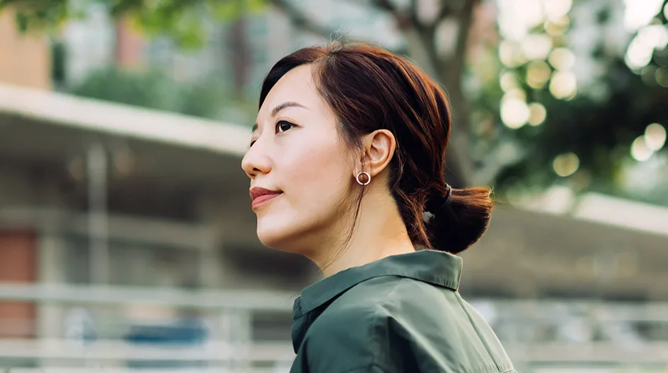 A woman relaxes outside a building on a leafy street.