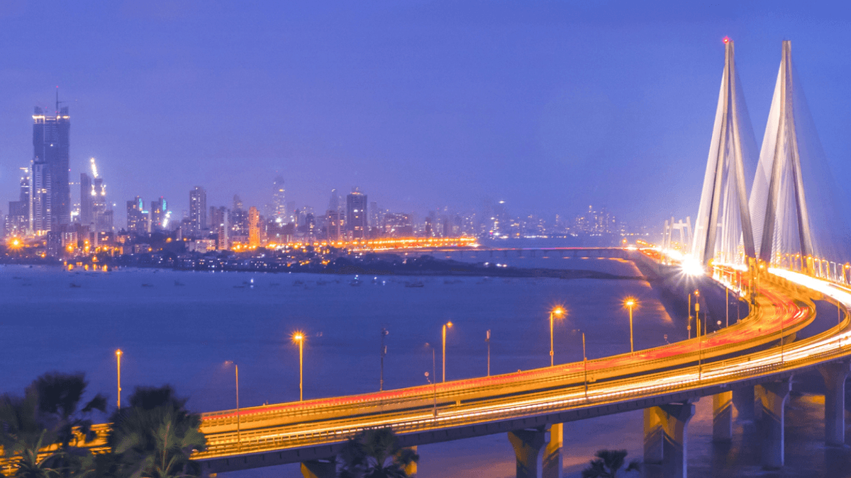 A bridge over the water leading to a bright city at night.