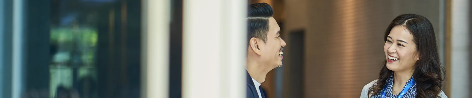 Two colleagues laugh together in a foyer.
