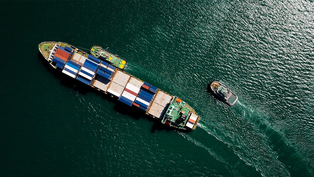 A container ship sails across a green sea.