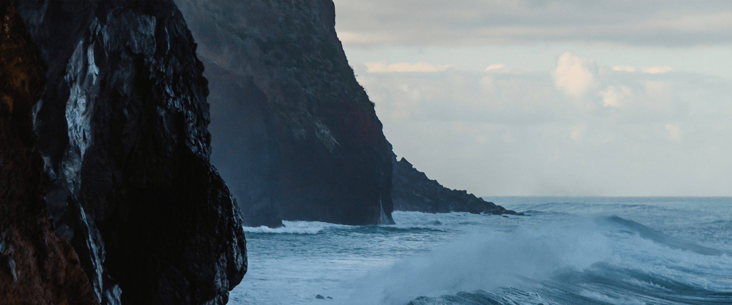 Waves hit a shore of rocky cliffs.