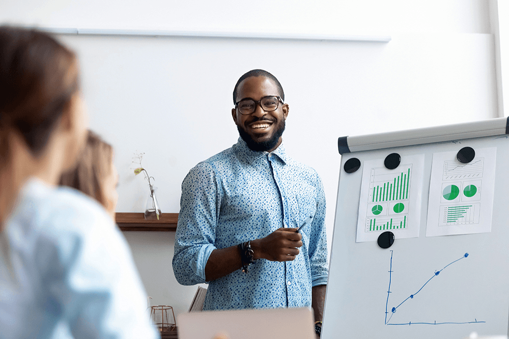 A man smiling and presenting charts on a white board