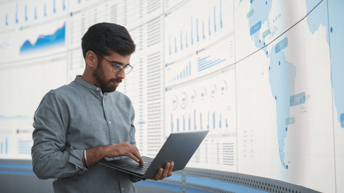 Man holds laptop, while working in front a digital global map