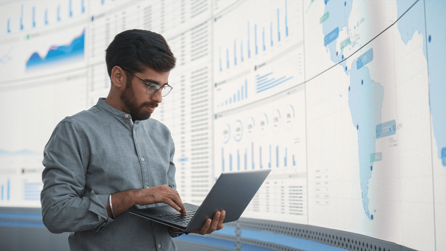 Man holds laptop, while working in front a digital global map