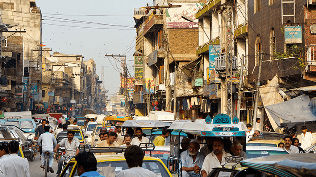 A narrow, busy road full of vehicles. Buildings are lined up on either side of the road