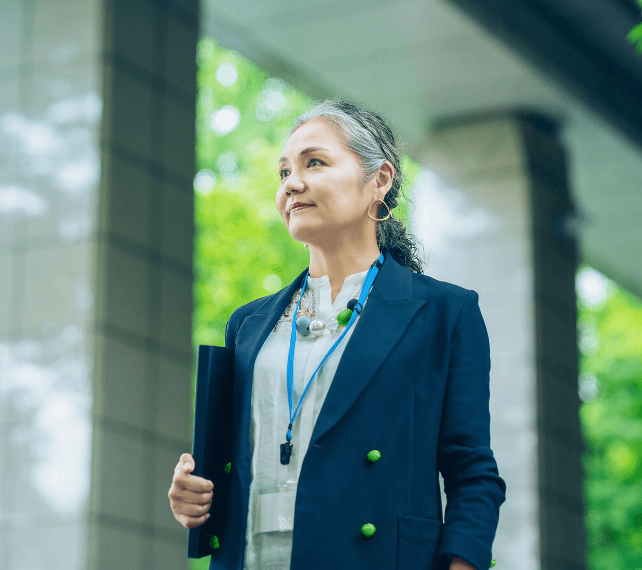 A woman stands with a file under her arm. She is in her 50s and wearing smart, executive clothing.