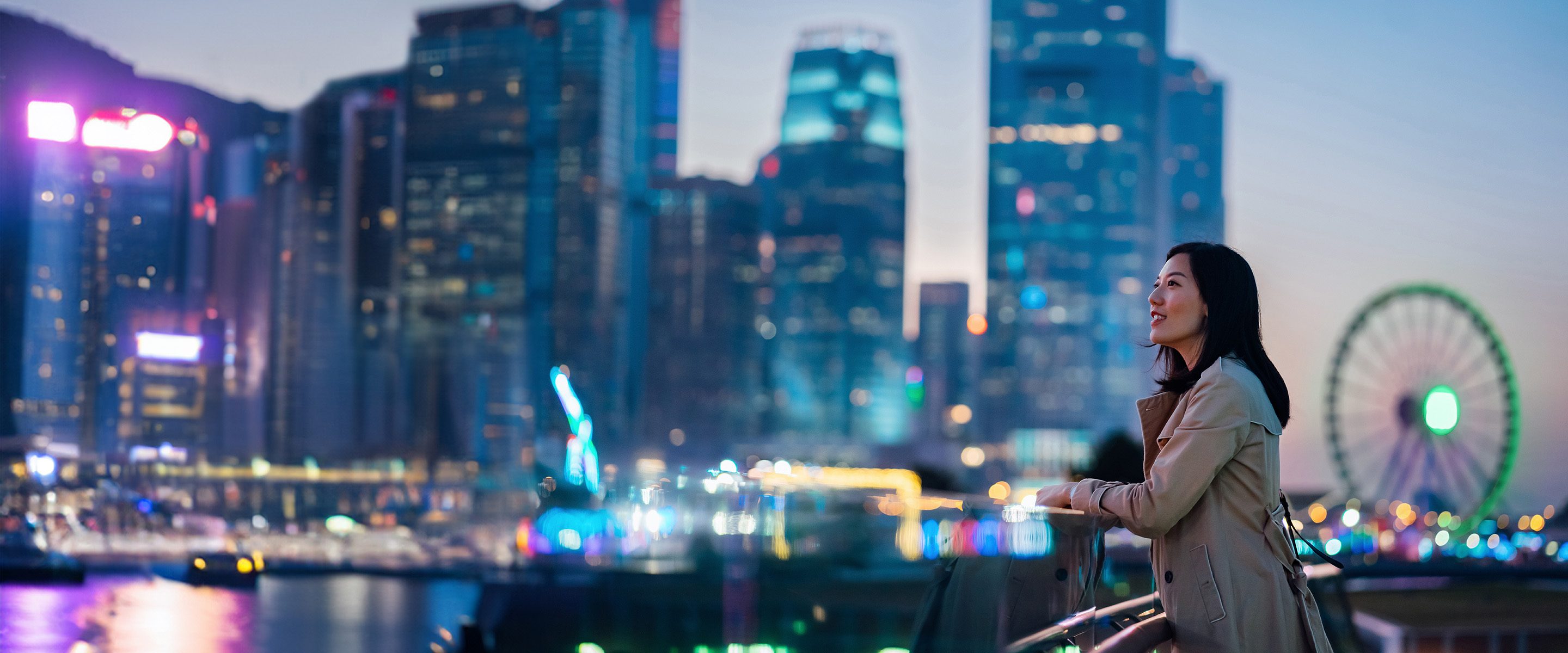Confident young Asian woman standing against illuminated city buildings