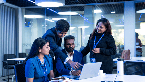 Three Standard Chartered colleagues gather around a laptop in an office, focused on their discussion and teamwork.