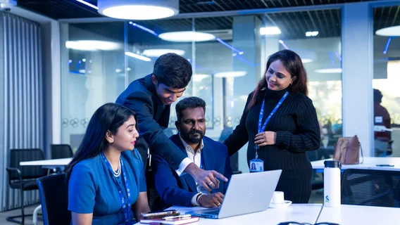 Three Standard Chartered colleagues gather around a laptop in an office, focused on their discussion and teamwork.