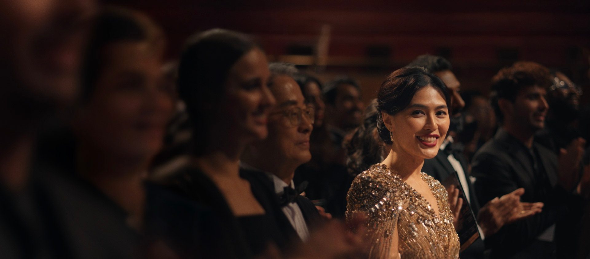 A woman in a sequined gold dress smiles at the camera.