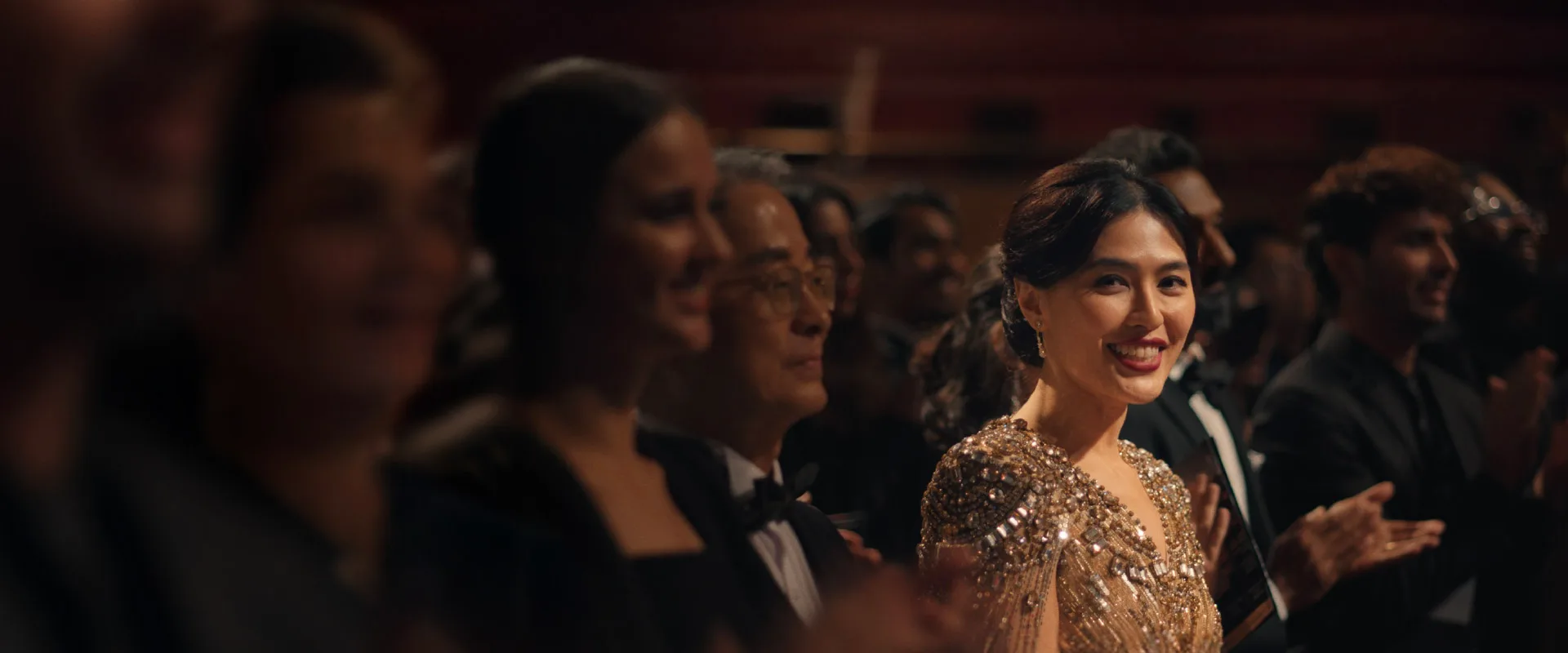 A woman in a sequined gold dress smiles at the camera.