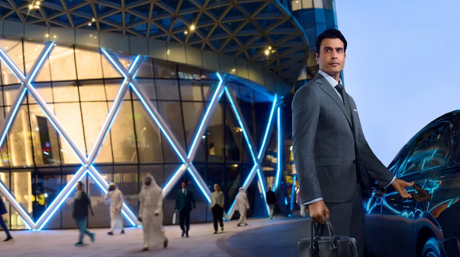 A man in a suit stands beside a luxury car