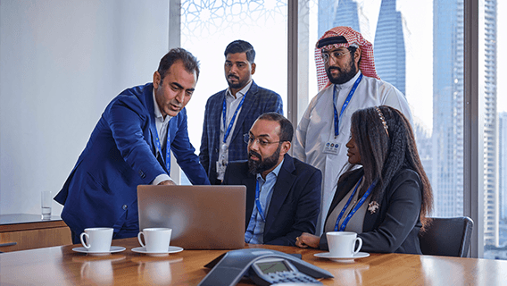 A group of Standard Chartered employees collaborate around a laptop.
