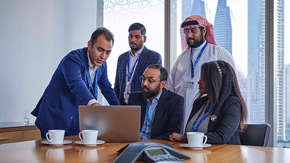 A group of Standard Chartered employees collaborate around a laptop.