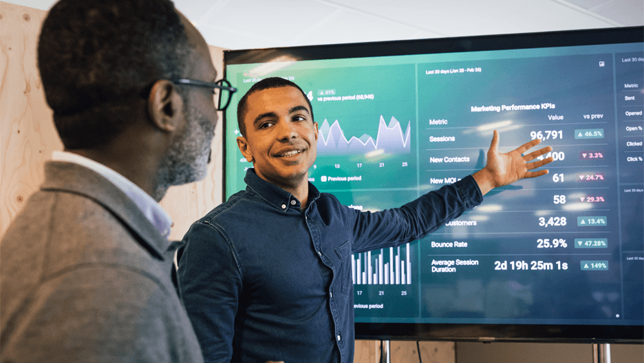 Two men analyze a large screen displaying various graphs and charts