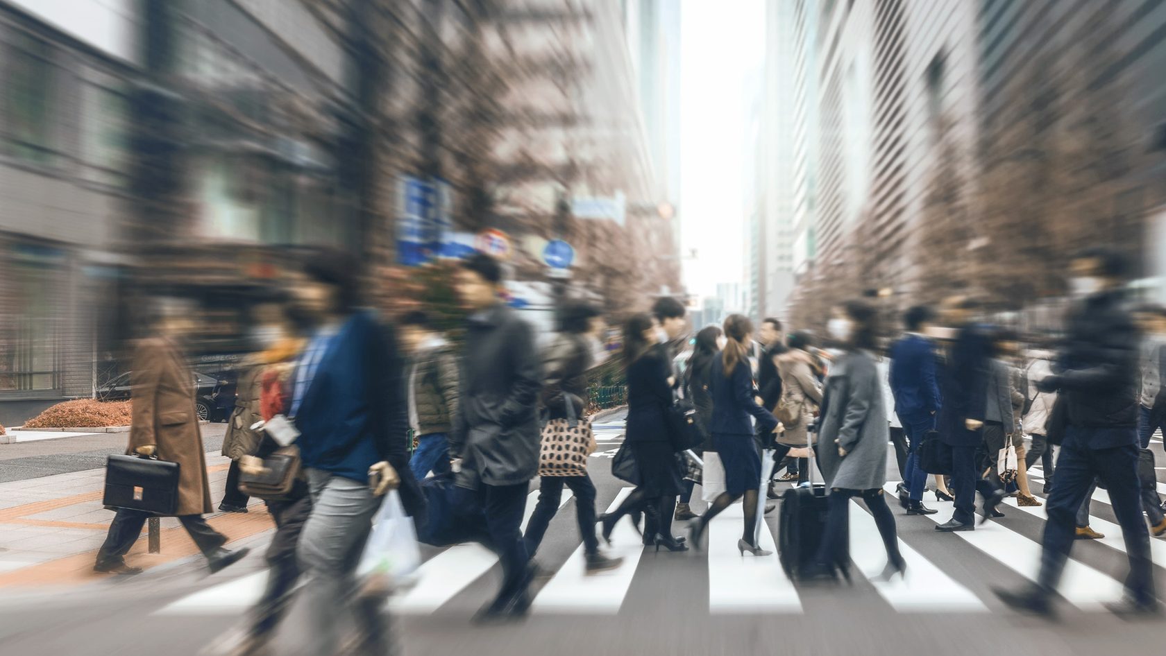 People walk across a zebra crossing in a busy urban street.