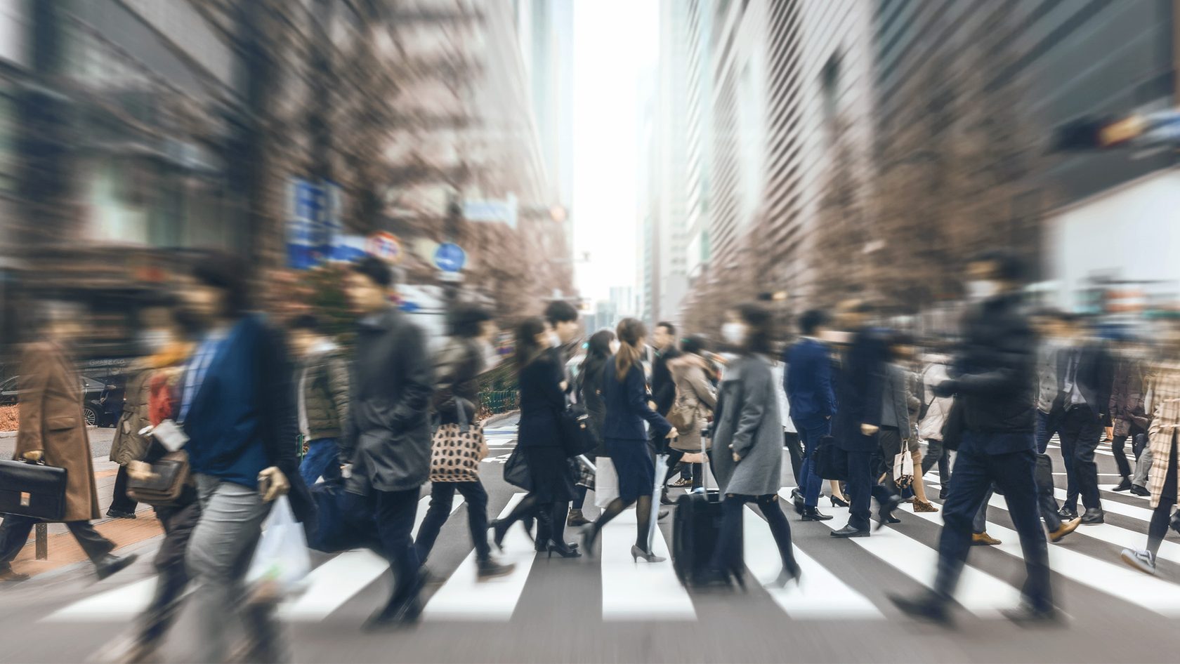 People walk across a zebra crossing in a busy urban street.