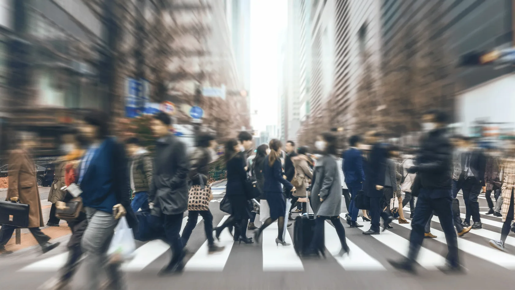 People walk across a zebra crossing in a busy urban street.