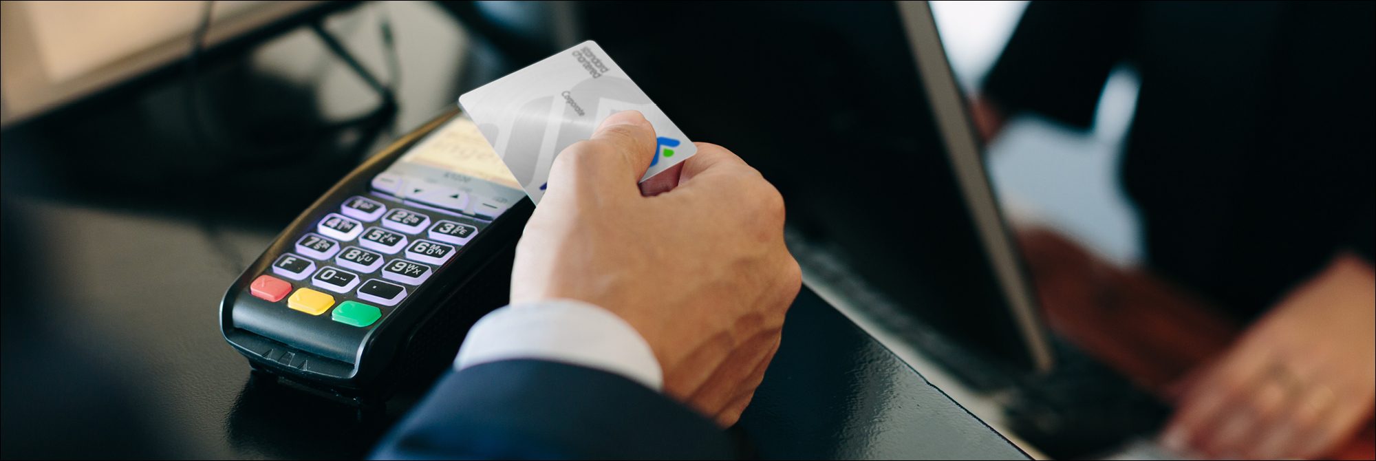 close up image of a hand holding a corporate credit card over a payment device