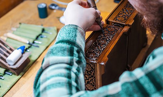 An artisan hand-carves a wooden box.