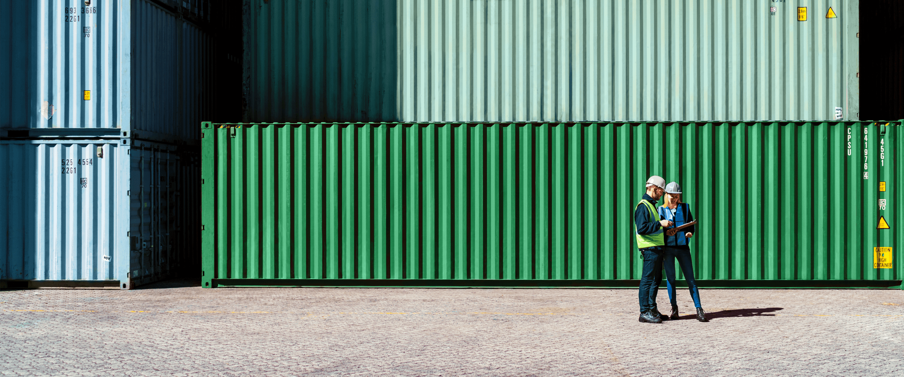 Two people review a document in front of shipping containers.