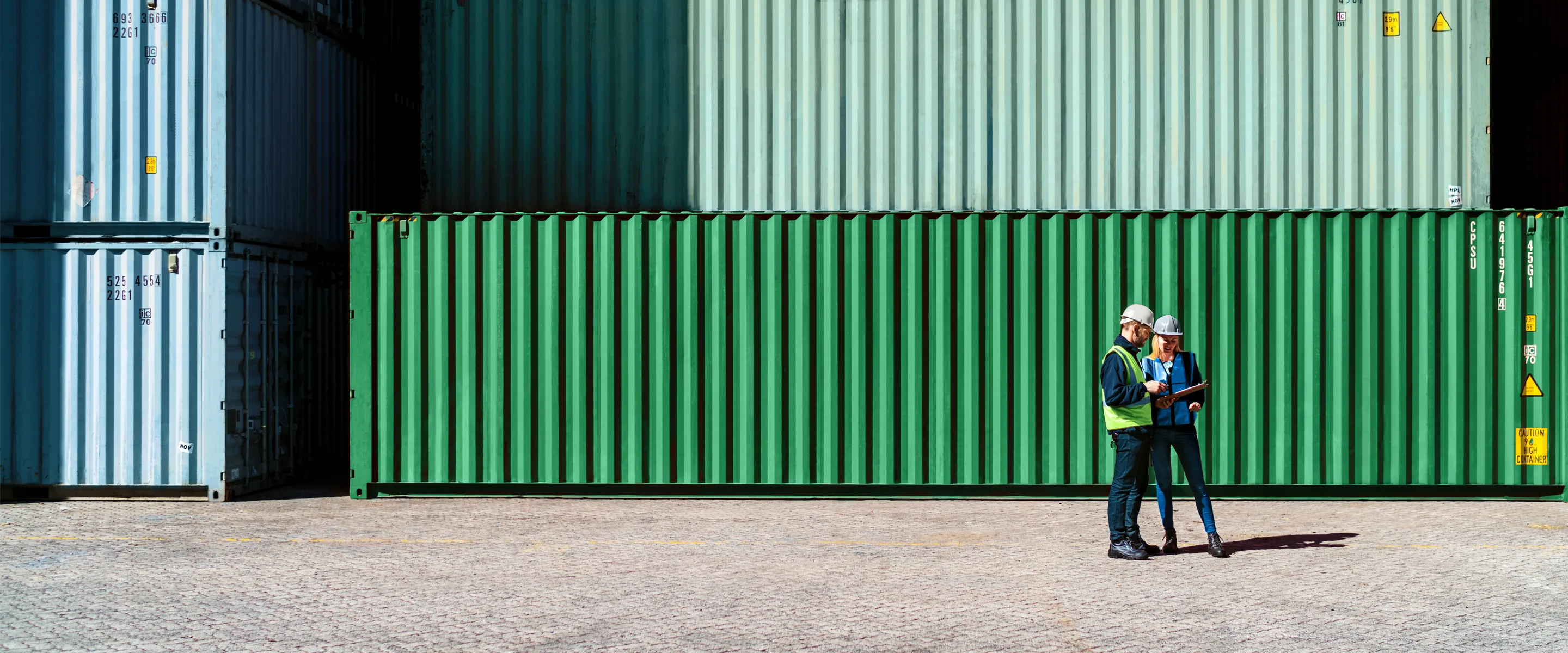 Two people review a document in front of shipping containers.