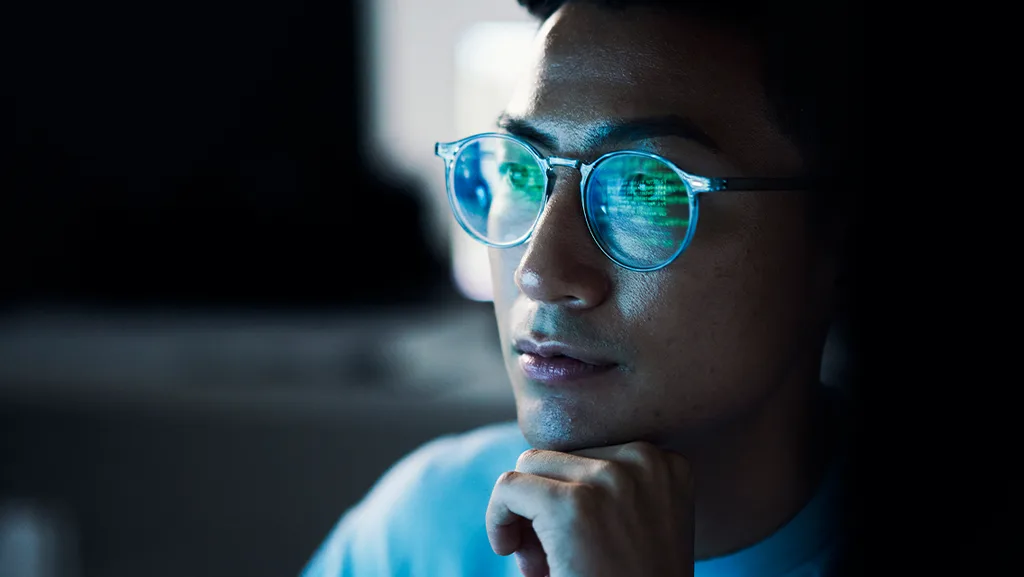 A man wearing a spectacle looking into a computer screen
