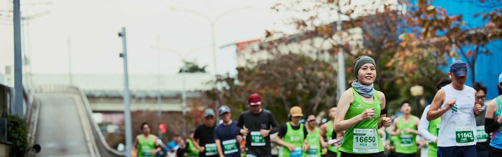 A smiling woman runs a marathon sponsored by Standard Chartered.