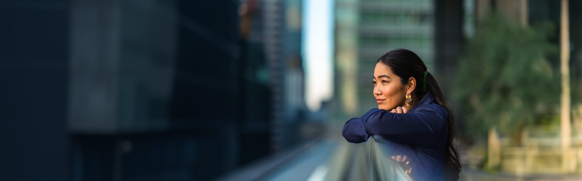 A woman leans against a railing, gazing at the city skyline in the background.