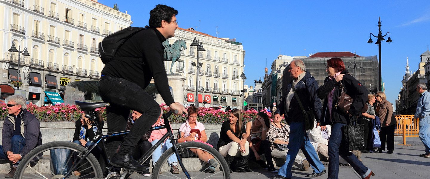 man riding bicycle past people sitting