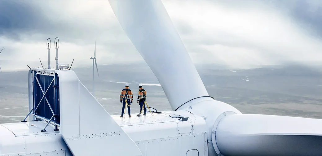 Two workers stand on a wind turbine.