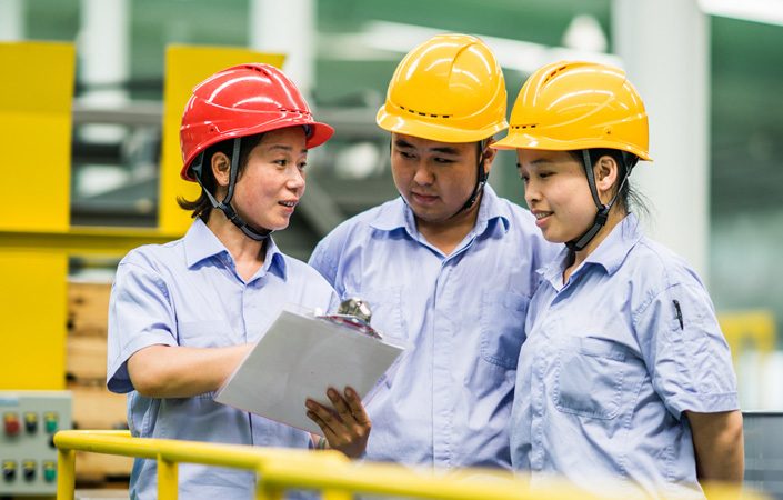 Three people in factory wearing hard hats