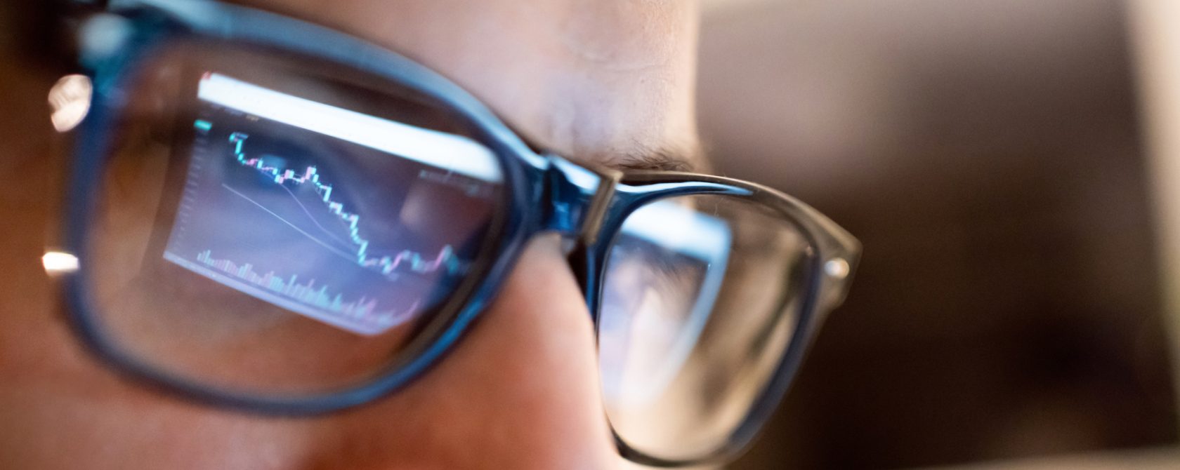 Closeup of a person's face with glasses reflecting a screen of the market