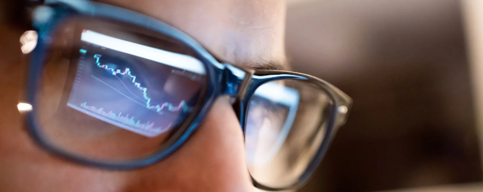 Closeup of a person's face with glasses reflecting a screen of the market