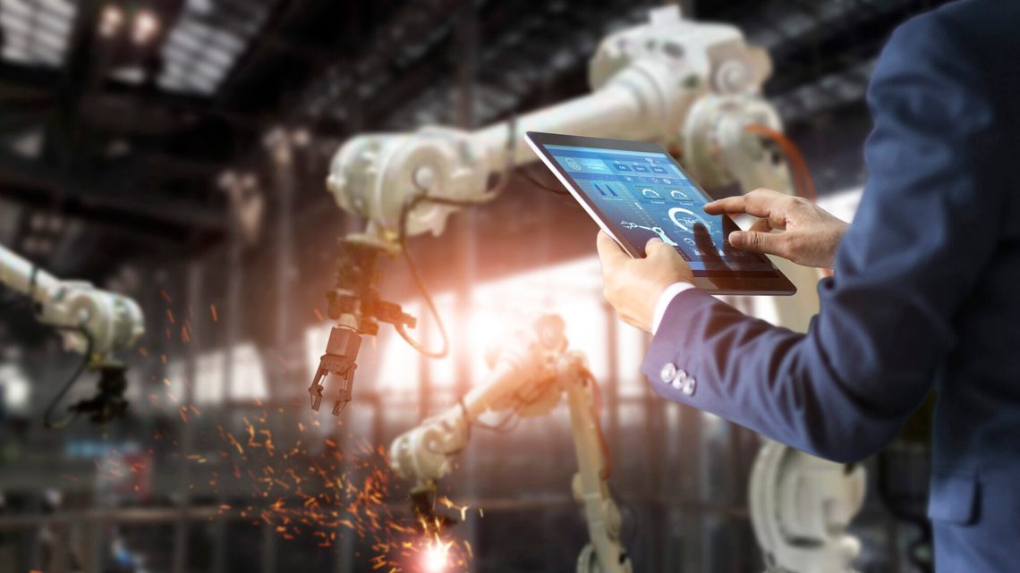 A man with an ipad in a factory operating a robot