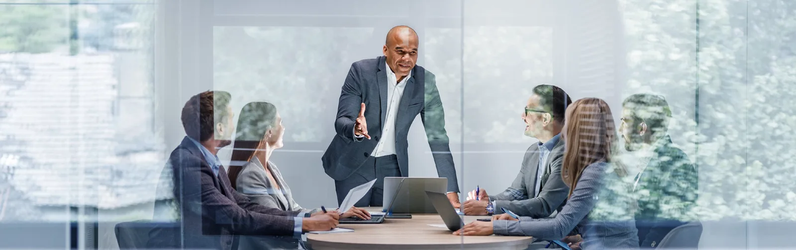 Man giving a presentation with laptop on the table for 5 people inside a meeting room