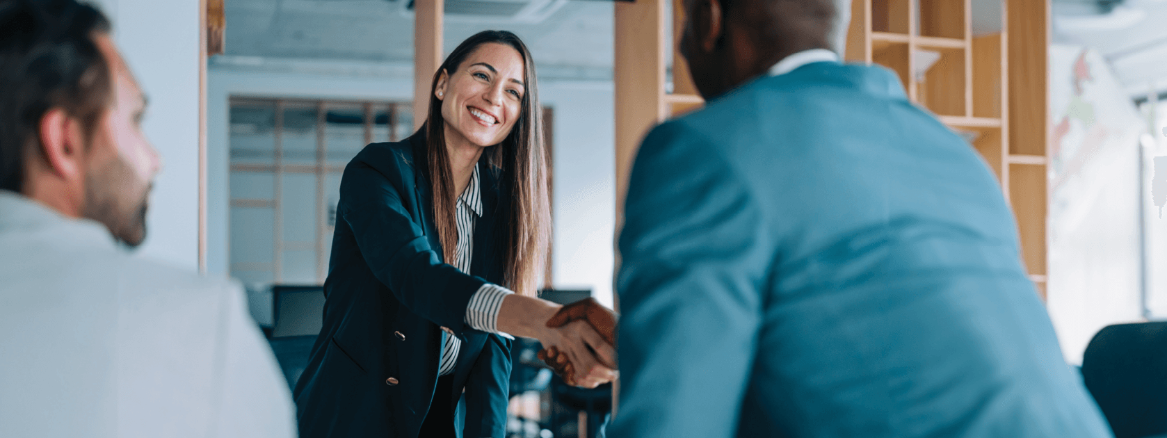 A woman in a suit smiles as she gives a hand shake to a man
