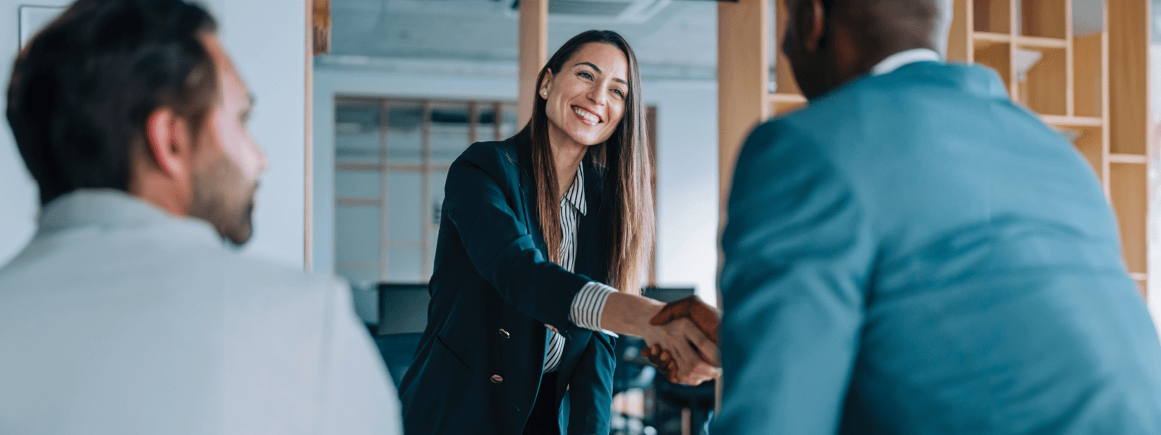 A woman in a suit smiles as she gives a hand shake to a man