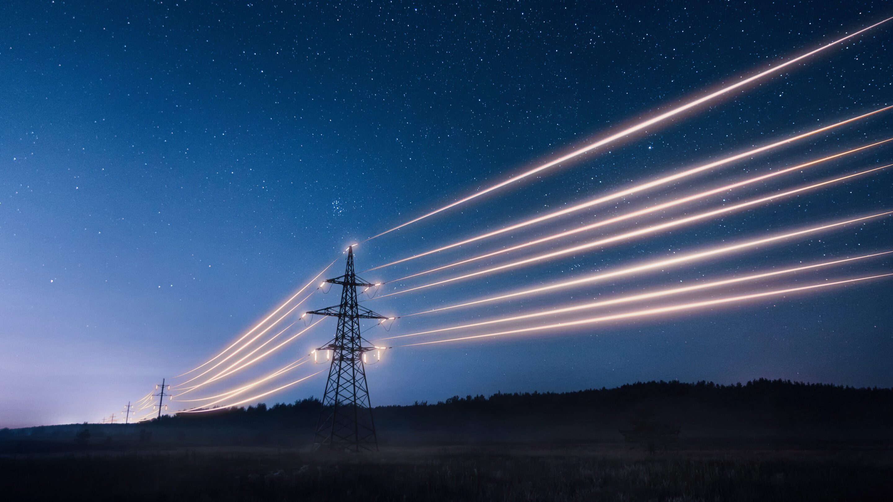 Power transmission lines illuminated against a starry night sky.